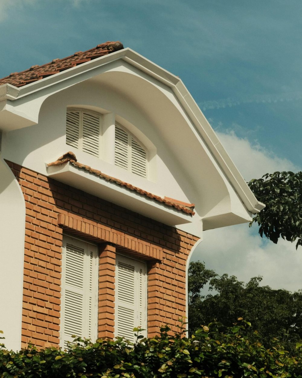 Exterior shot of a brick house featuring an arched roof and white shutters, set against a blue sky.