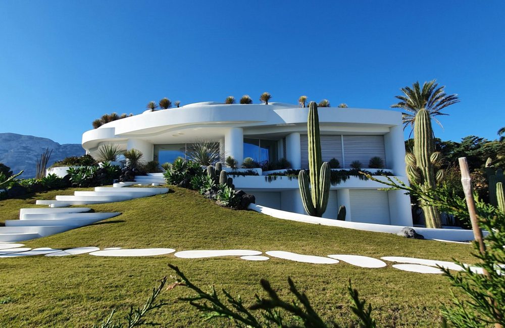Contemporary white villa with garden and cacti in Dénia, Spain under a clear blue sky.